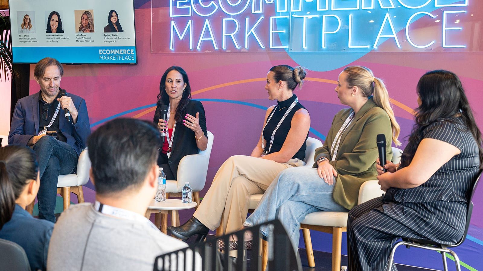 A moderator and four panellists on the Ecommerce Marketplace stage under its neon sign