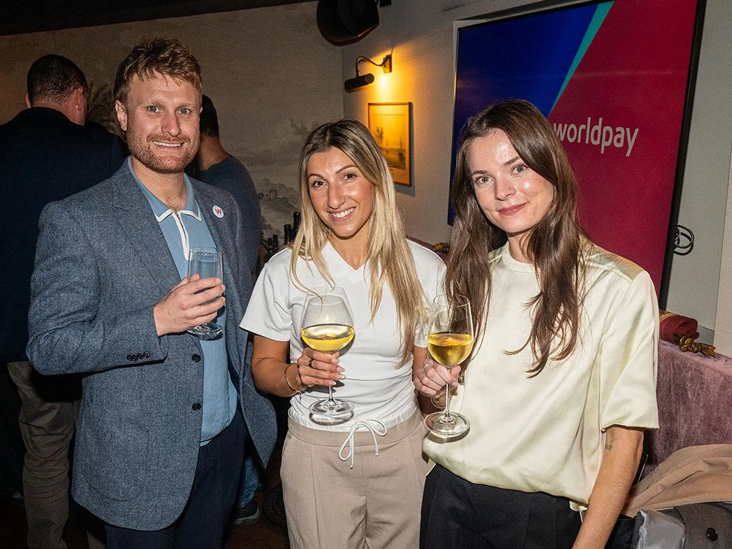 Three guests with drinks in front of a Worldpay screen at The Gidley