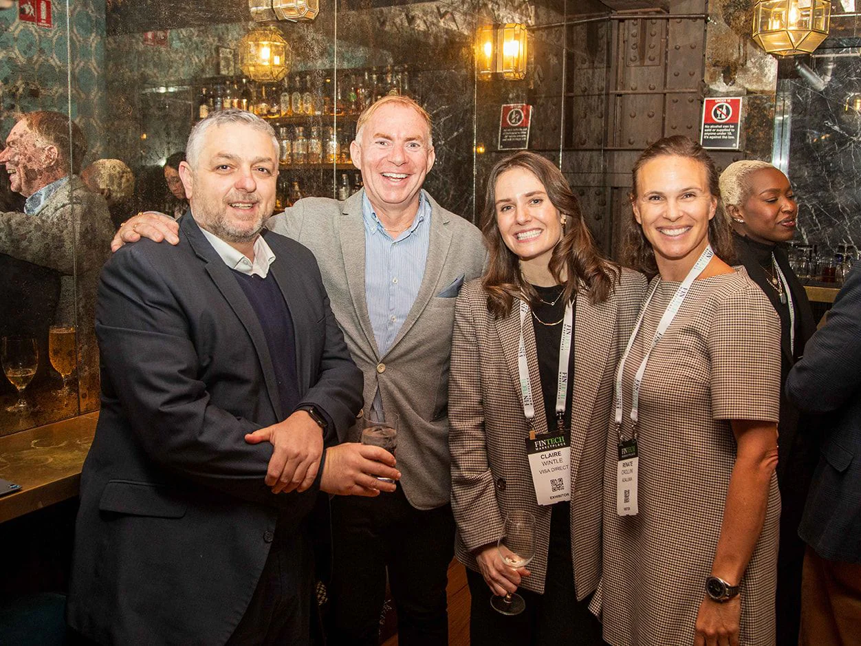 Four guests smiling together at a networking evening in a lamp-lit bar