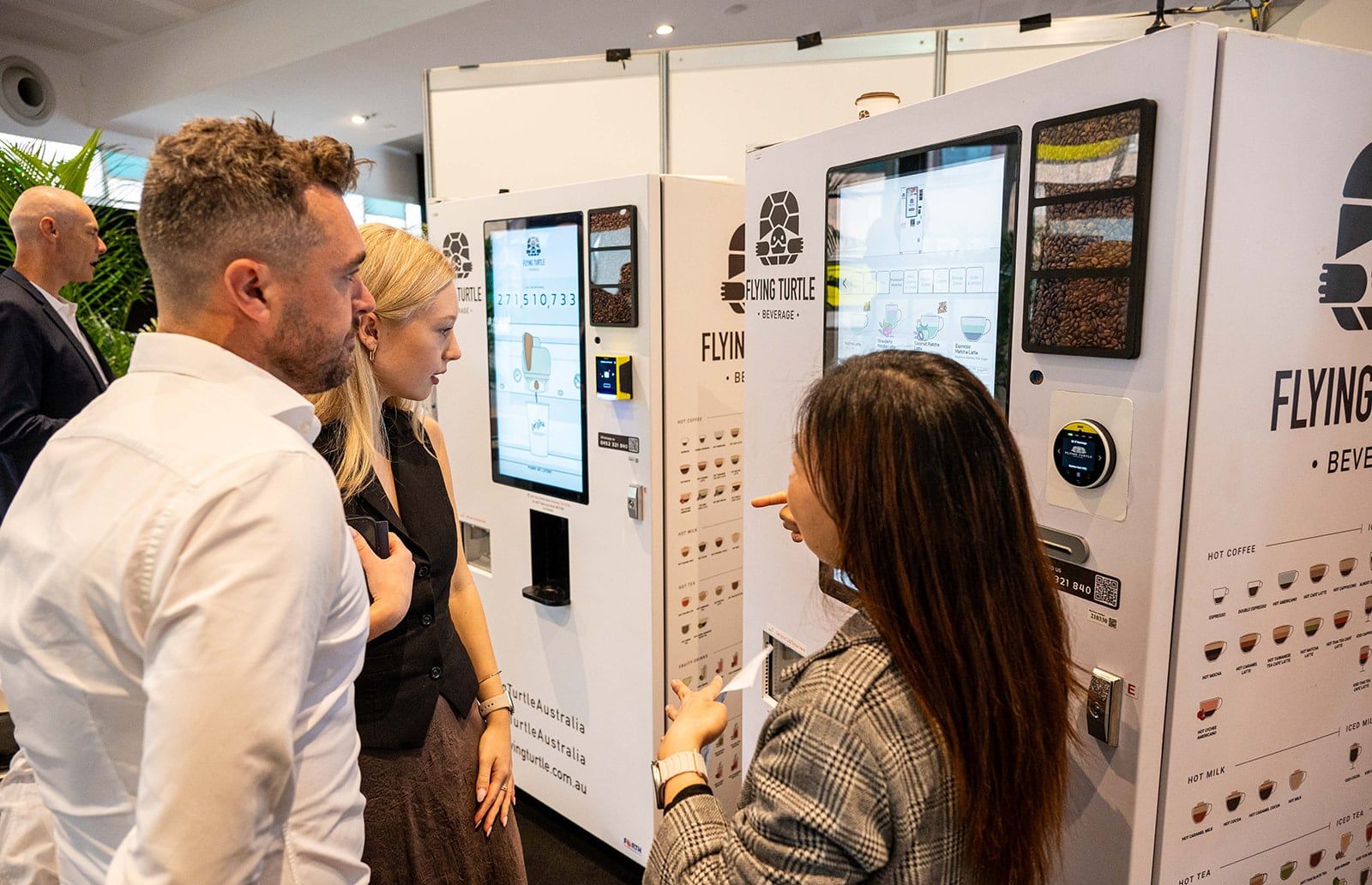 Two exhibitors and a visitor talking at a blue branded stand with a round counter and a large screen