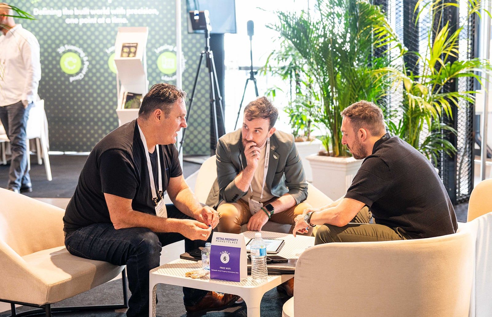 Three people in conversation around a low table on lounge chairs, with palms behind them
