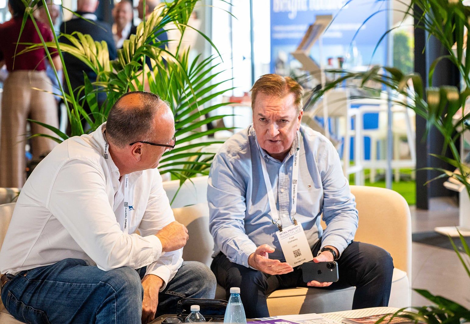 Two delegates in conversation on a cream lounge sofa among palms