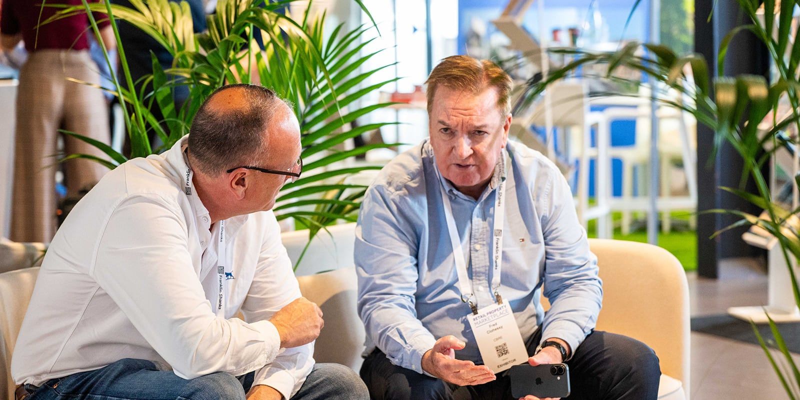 Two delegates wearing event lanyards and name badges talking on a lounge at the event