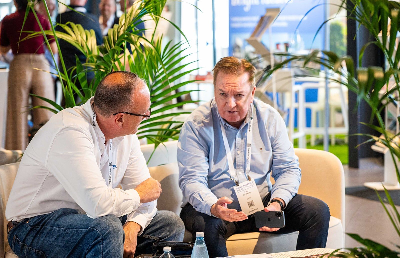 Two delegates in conversation on a cream lounge sofa among palms