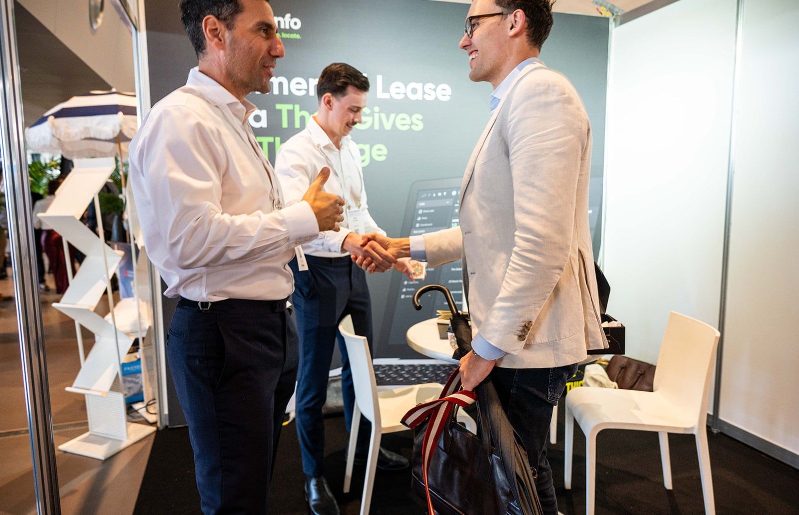 Three men in conversation, two shaking hands, at a commercial lease data stand