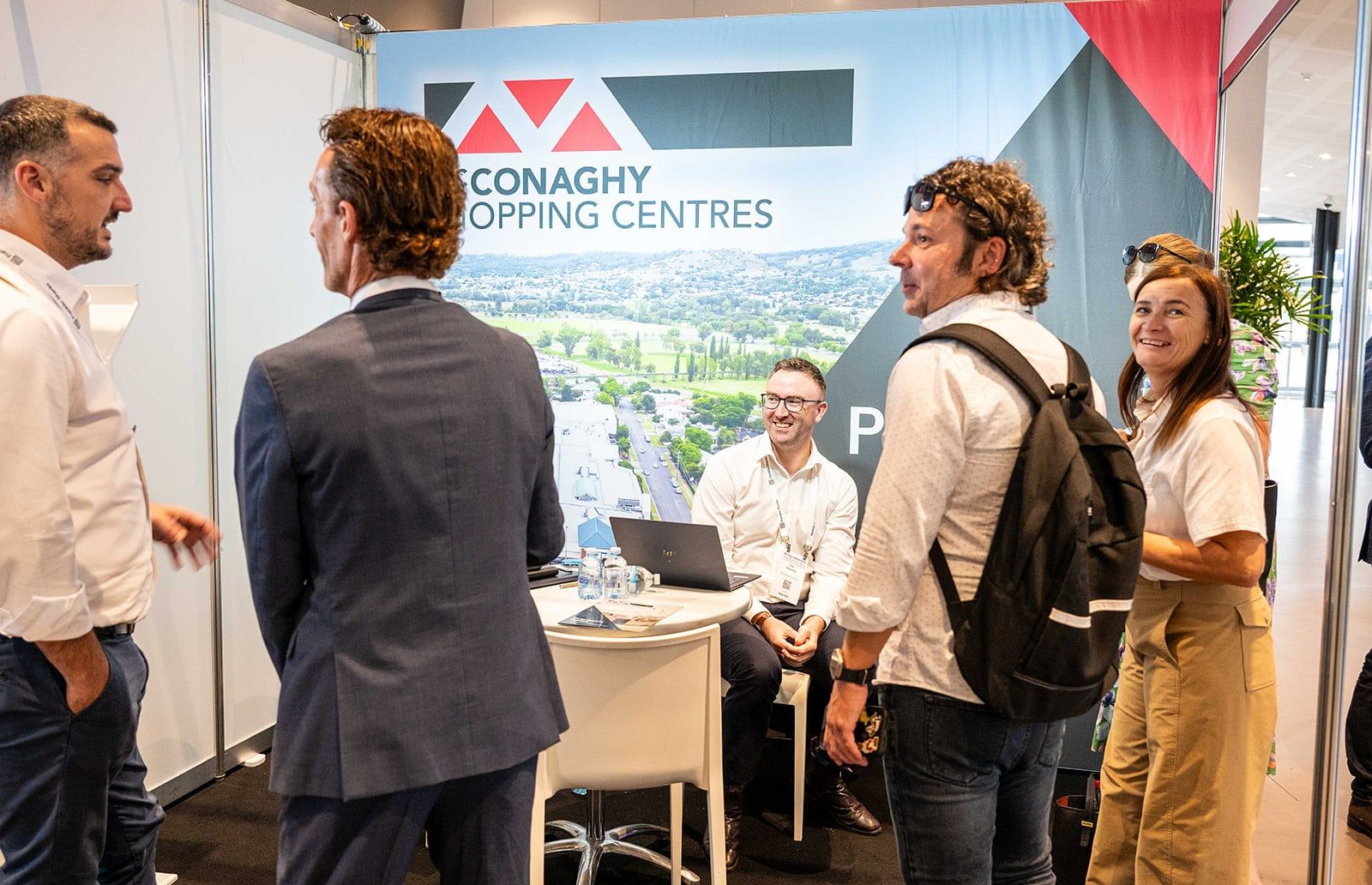 Visitors talking with the exhibitor team at a shopping centres stand with an aerial town photo