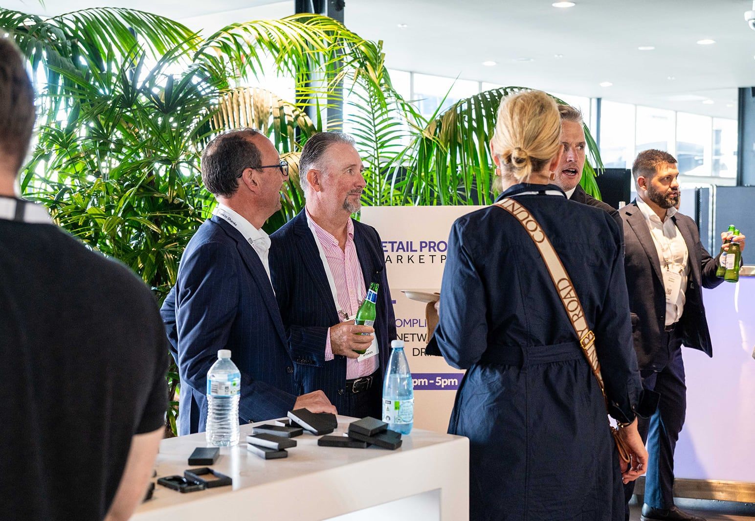 Delegates talking with drinks in hand beside the networking drinks sign, with palms behind