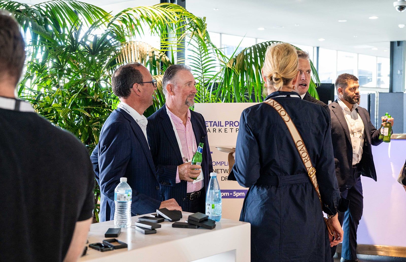 Delegates talking with drinks in hand beside the networking drinks sign, with palms behind