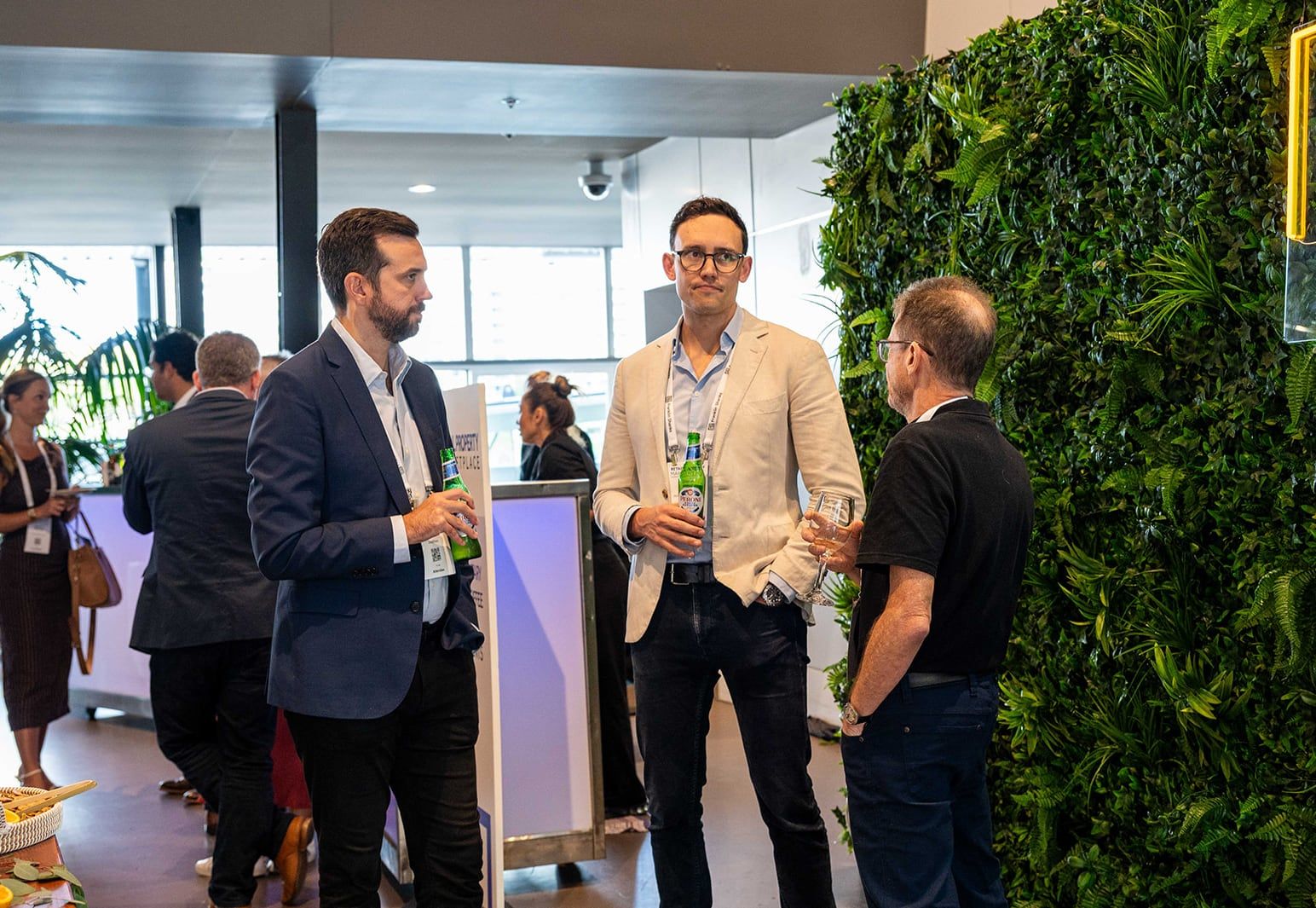 A group of delegates talking over drinks beside a green wall
