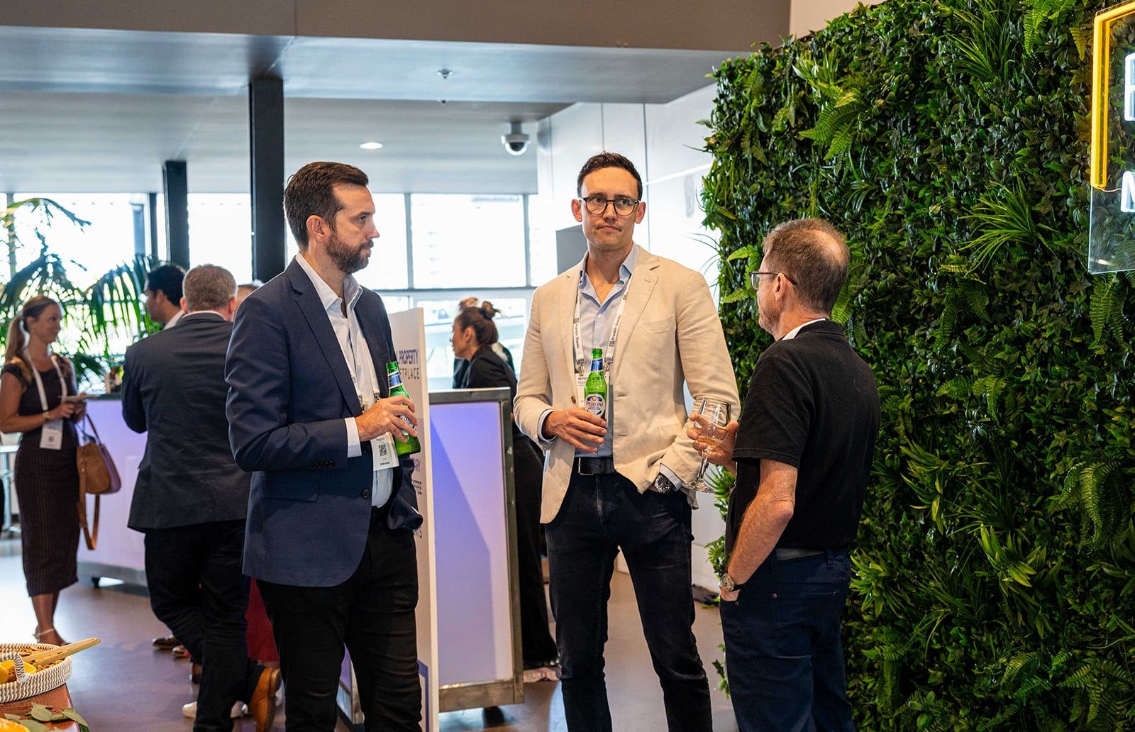 A group of delegates talking over drinks beside a green wall