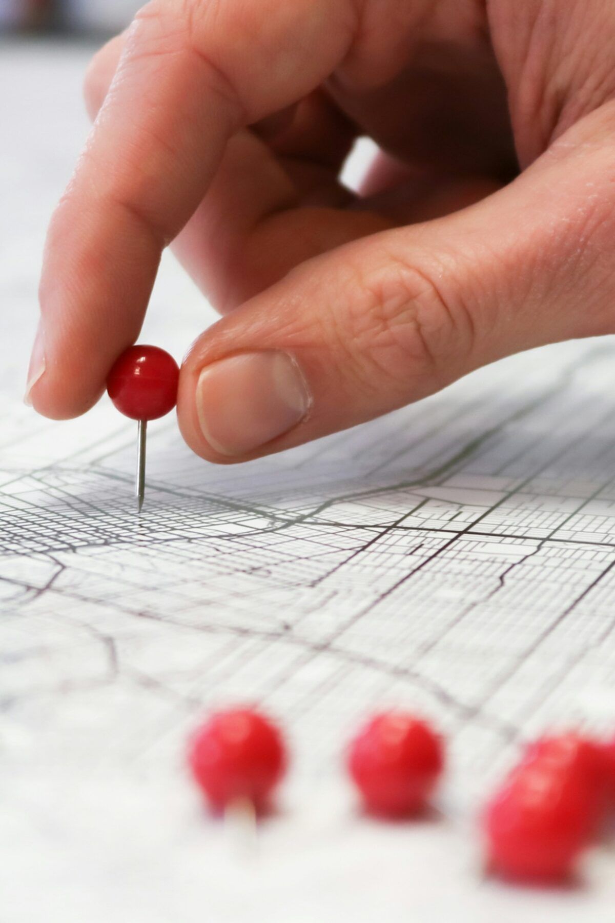 A hand pressing a red pin into a street map, with more red pins waiting in the foreground