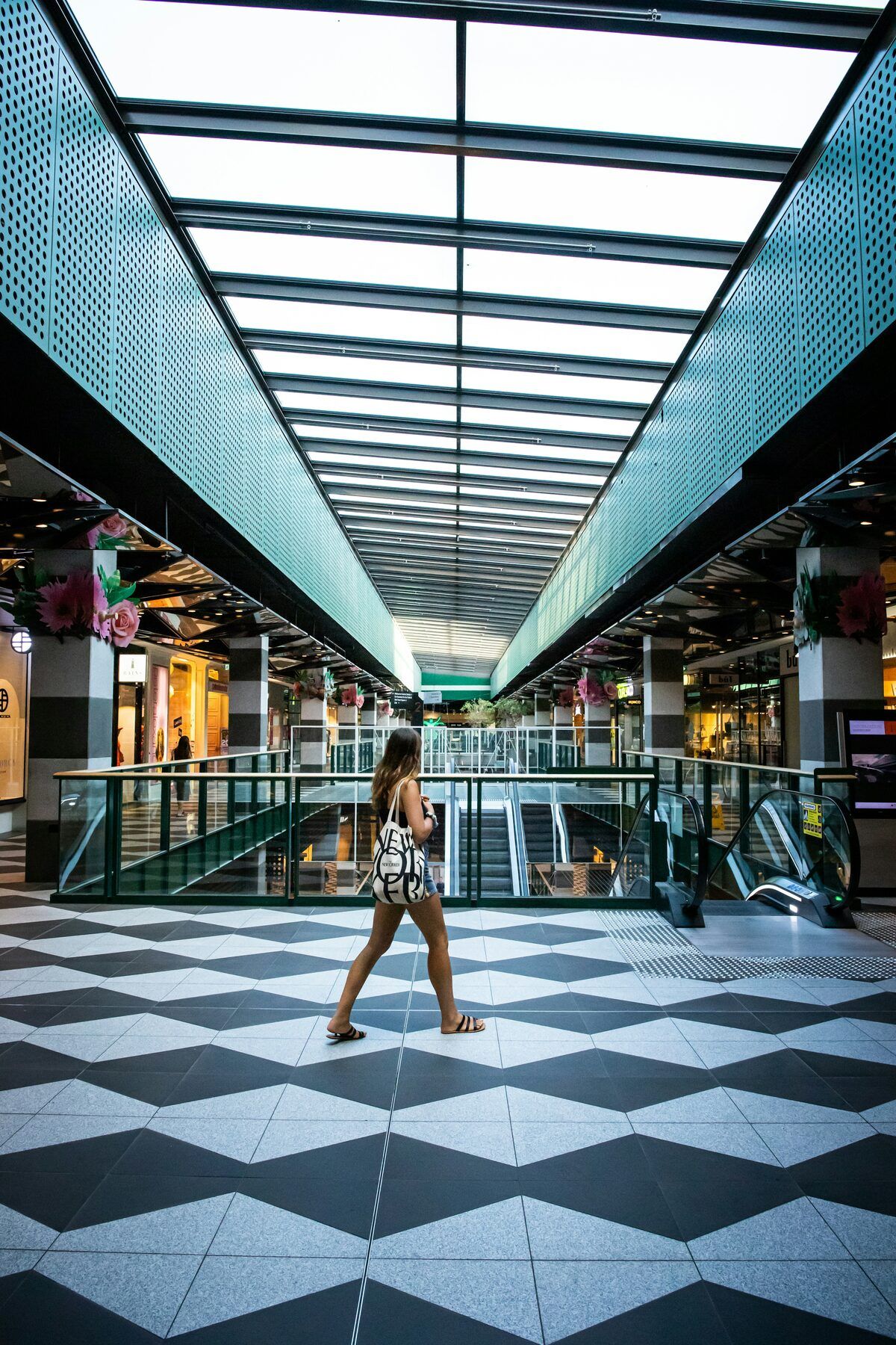 A shopper walking through a shopping centre concourse beneath a glass skylight