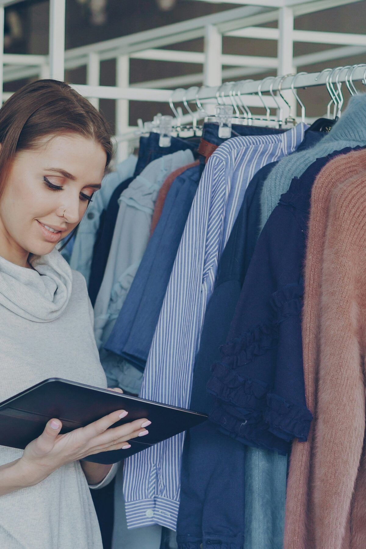 A woman checking a tablet beside a rack of clothes