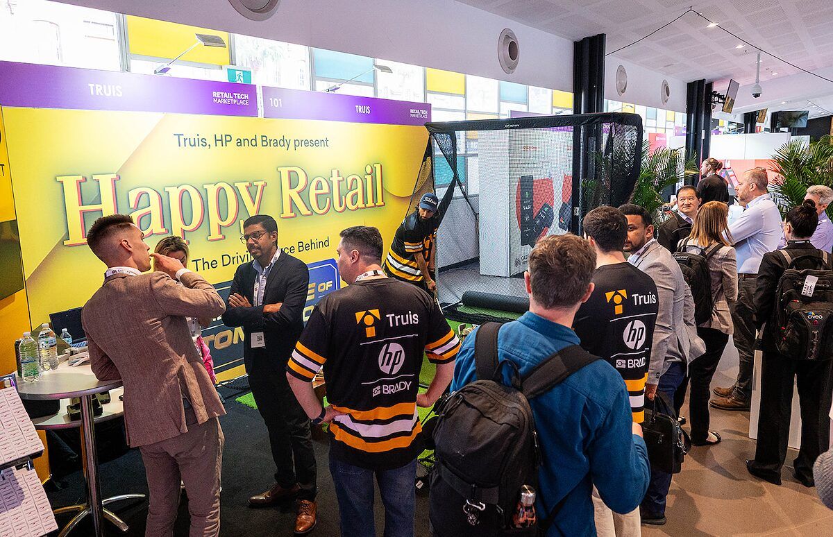 Visitors gathered around a brightly branded exhibitor stand with a large retro-style display
