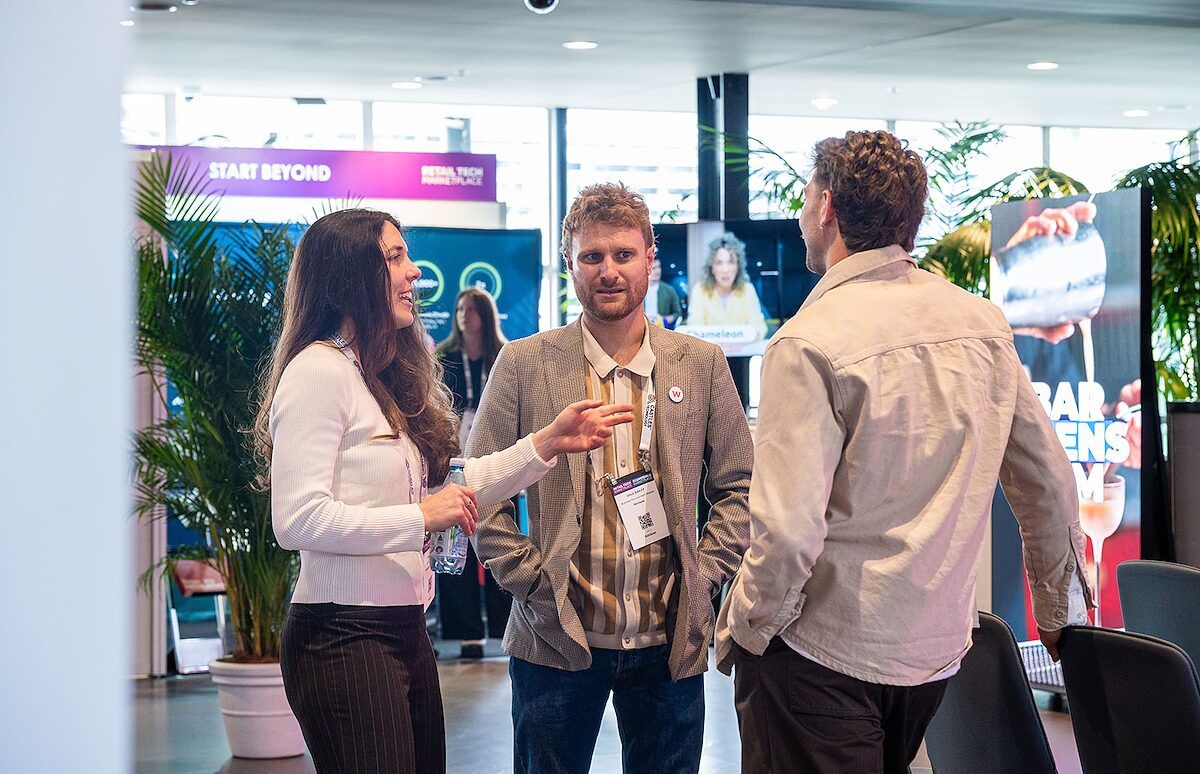 Three people chatting in the event hall, with palms and signage behind them