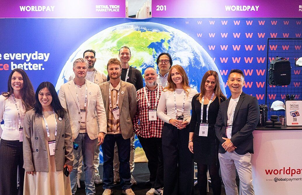A large exhibitor team posing together in front of a payments stand