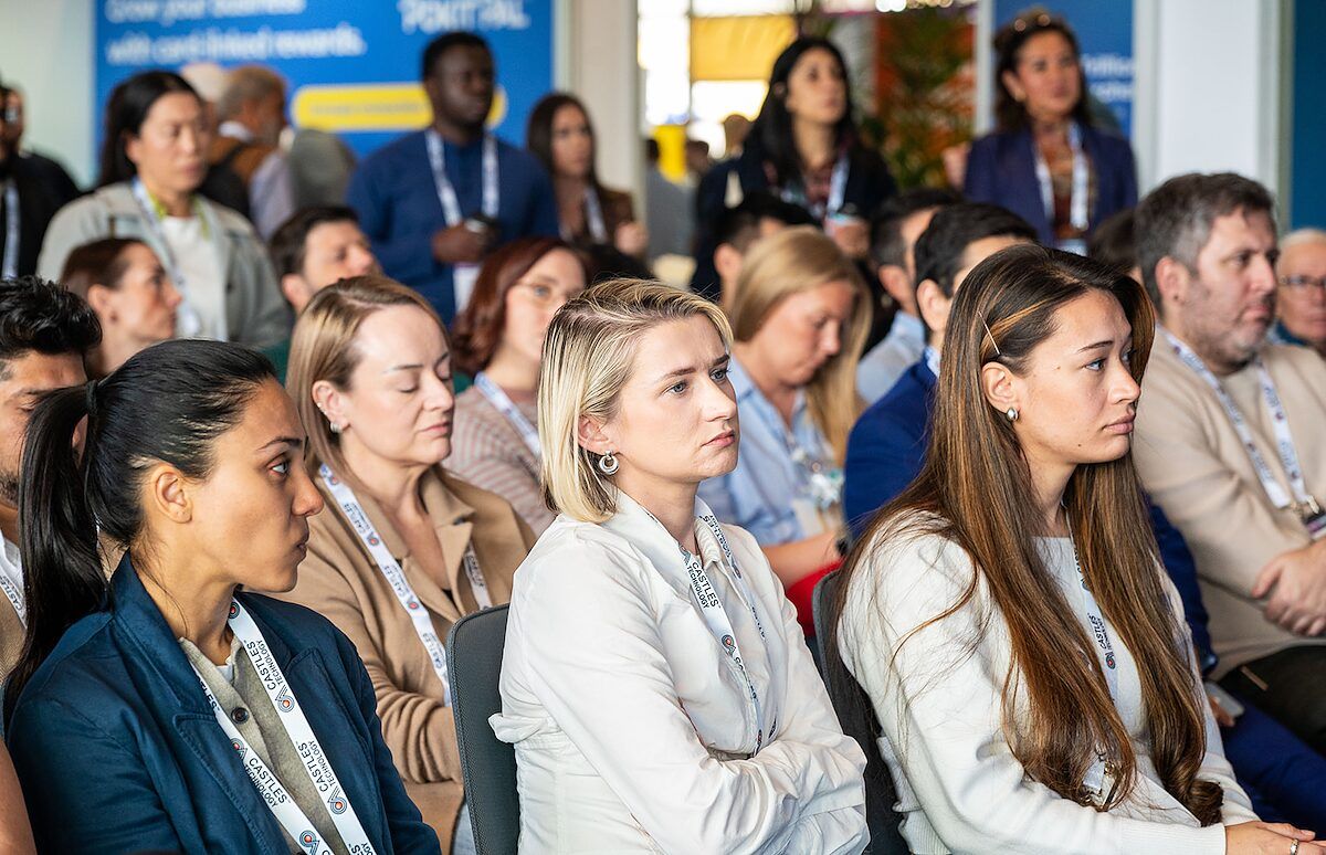 An audience seated and listening intently to a session, with lanyards around their necks