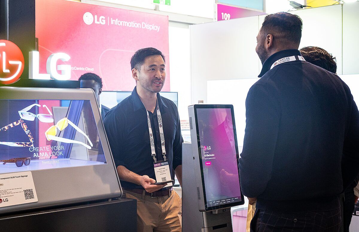 An exhibitor talking with a visitor beside a large interactive display at an LG stand