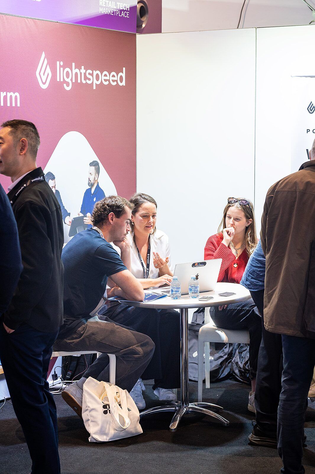 An exhibitor and visitors in a working meeting around a table beside a stand