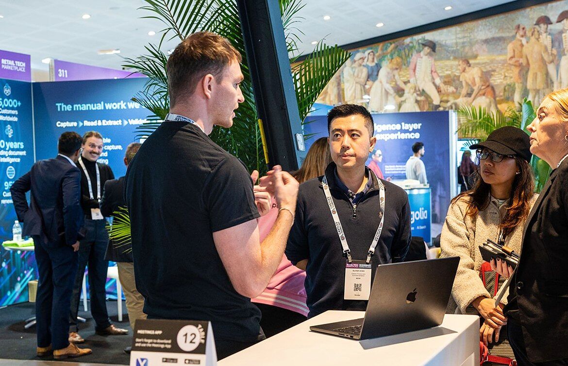 An exhibitor demonstrating a laptop to two visitors at a stand