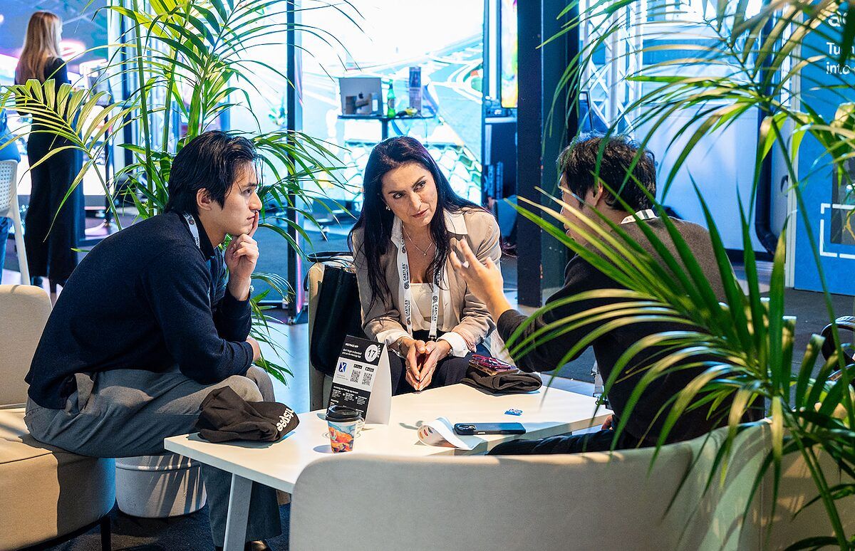 Three people in conversation at a low table among plants in the event lounge