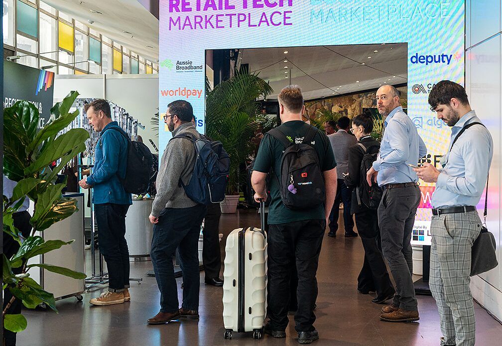 Attendees arriving and talking under the Retail Tech Marketplace entrance arch