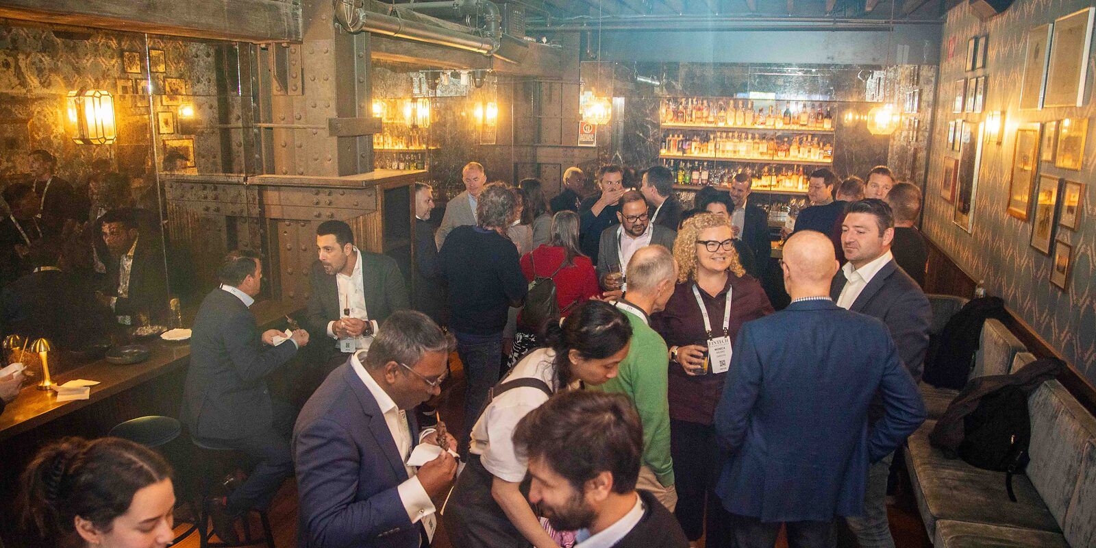 Guests talking over drinks in a warmly lit bar at the event afterparty