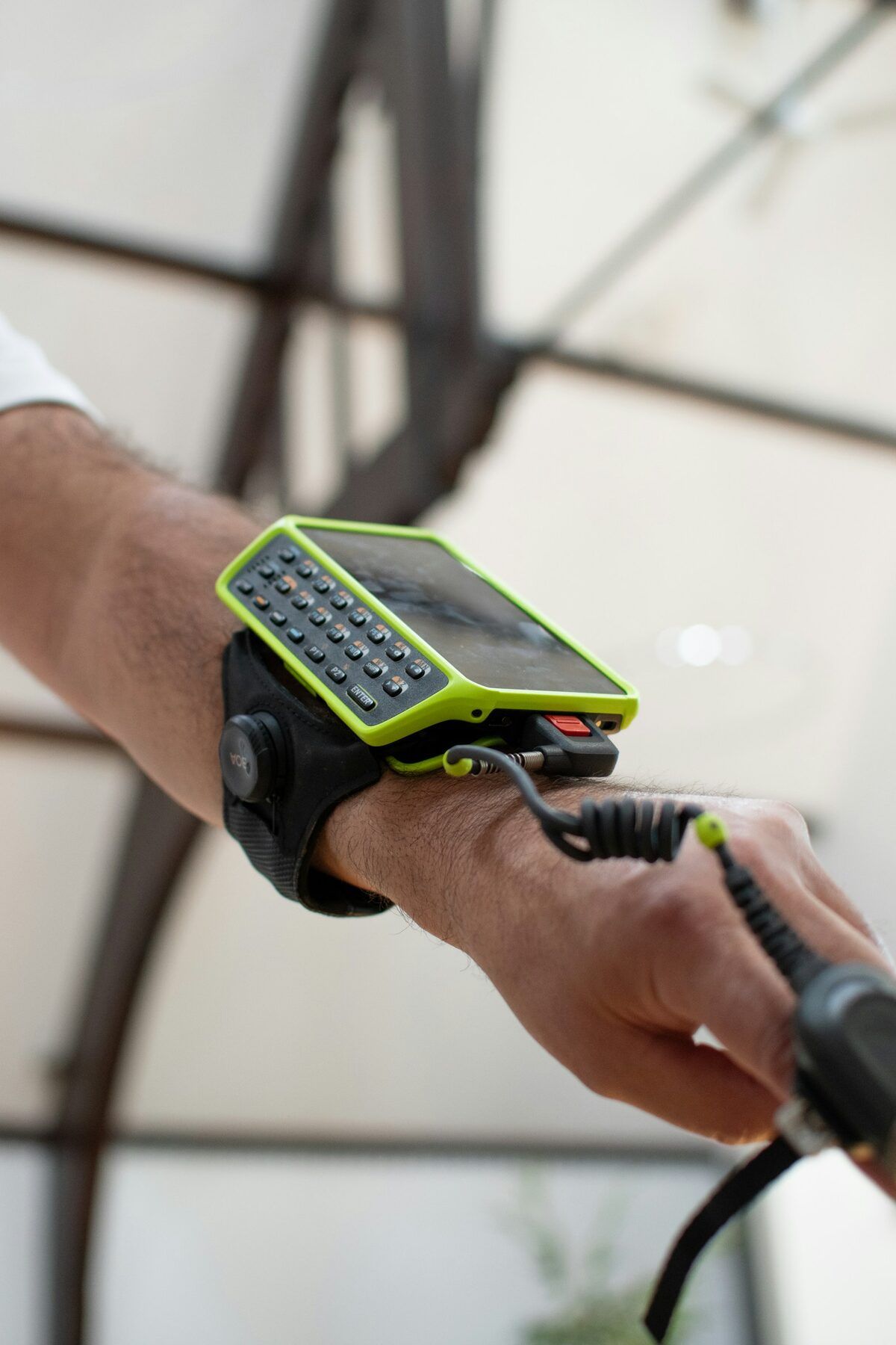 A rugged handheld computer with a keypad strapped to a forearm, cabled to a hand scanner